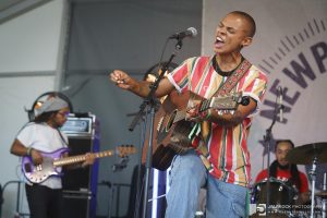A singer/guitarist in a bright striped shirt onstage at Newport Folk Festival as part of the Black Opry set