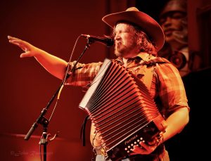 Willi Carlisle plays accordion onstage and points toward the crowd