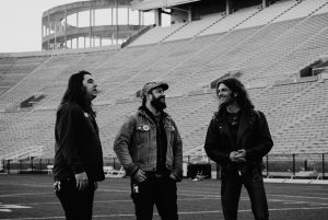 Lee Bains and two bandmates on the field of a large football stadium