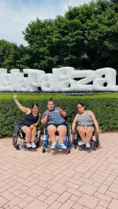 Three women in wheelchairs in front of an inflatable Lollapalooza sign