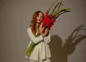Bella White in cream suit holding a bouquet of red flowers