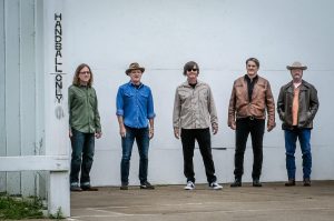 The five members of Son Volt lined up against an exterior white wall