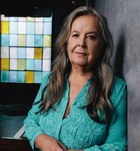 Tracy Nelson in teal blouse with a stained glass window in the background