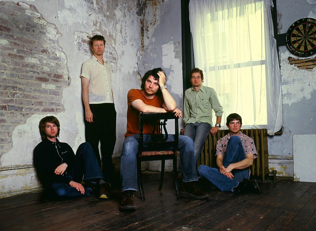 A early photo of the five members of Wilco in the corner of a shabby room